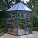 8 ft Oasis hex greenhouse installed in a garden with plants and paved base