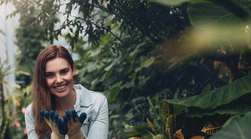 A smiling person in a gray sweater among green foliage.